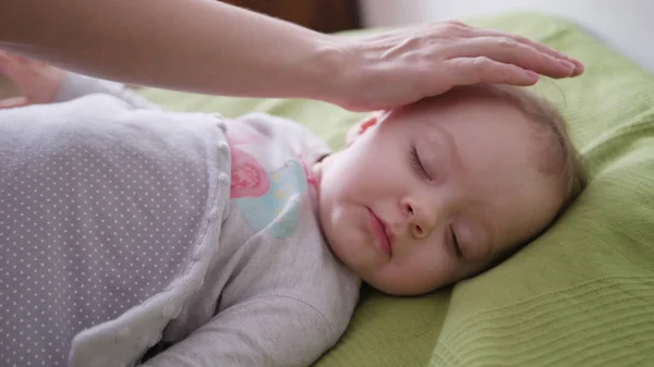 Kvinnliga händer som täcker en bebis i sängen — Stockfoto