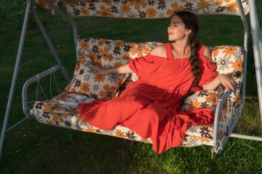 Kırmızı elbiseli bir genç kız bir ülke salıncakta dinleniyor