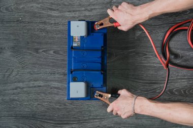 Erkek el terminalleri ahşap arka plan üzerinde araba pil bağlanır