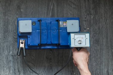 Bir adamın elini bir araba pil test eden bir ahşap arka plan üzerinde tutar.