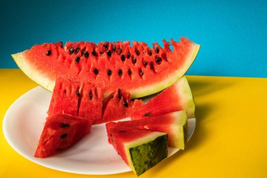 Sarı ve mavi zemin üzerine beyaz bir tabakta karpuz yalan dilimlenmiş