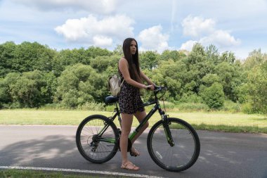 Kız bir bisiklet sürme. Yan görünümü. Orman ve arka planda bulutlar