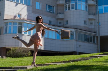 Modern bir kız elbise, gözlük ve bir çanta yol üzerinde atlar. Mutluluk ve başarı duygu. Modern genç iş kadını