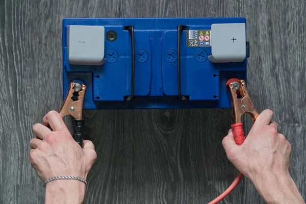 De mannenhand verbindt de terminals aan de auto's batterijen op een houten achtergrond — Stockfoto