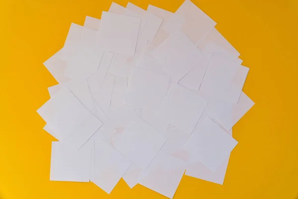 White square paper pieces spread out in chaotic order on a yellow background — Stock Photo, Image