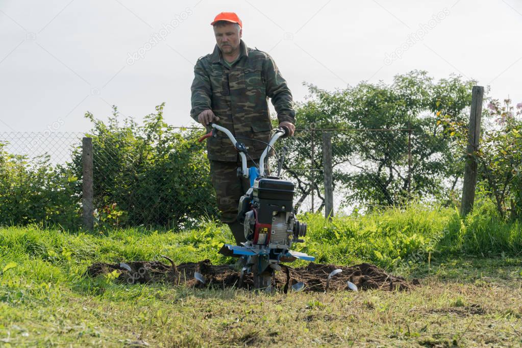 A man digs a garden with a cultivator