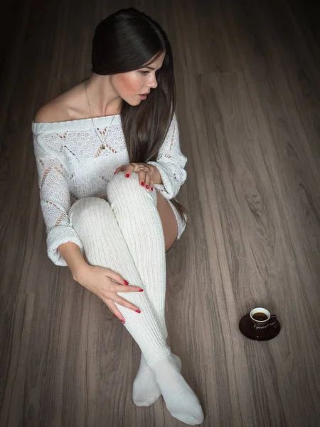 Mädchen mit weißem Pullover und Socken sitzt auf einem Holzboden mit einer Tasse Kaffee — Stockfoto