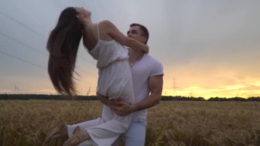Bir adam onun kollarında bir kızla bir buğday alanında günbatımında dönüyor. Ağır çekim