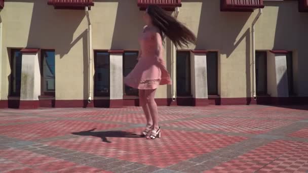 Een meisje in een roze jurk draait op de binnenplaats. Slow motion picture opname — Stockvideo