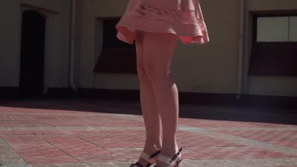 Egy lány, egy rózsaszín ruhás forog az udvaron. A kamera mozog a lábát a lány, és a fogások az ég. Lassú mozgókép felvétel — Stock videók