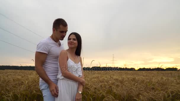 Um cara está beijando uma garota em um campo de trigo ao pôr do sol — Vídeo de Stock