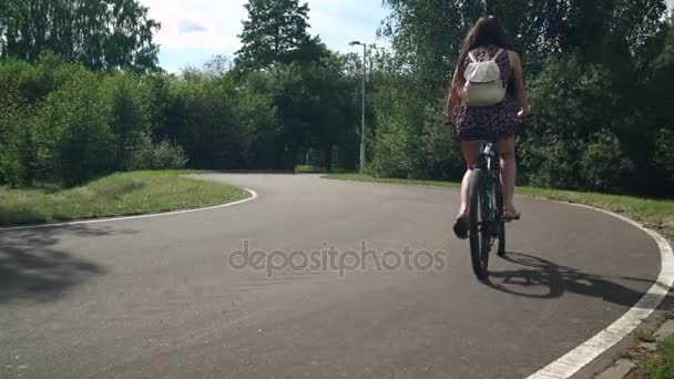 Uma rapariga a andar de bicicleta. Vista lateral. Floresta e nuvens no fundo — Vídeo de Stock