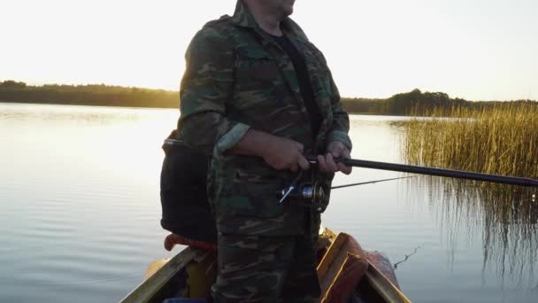 Un hombre está pescando desde un barco al atardecer — Vídeos de Stock