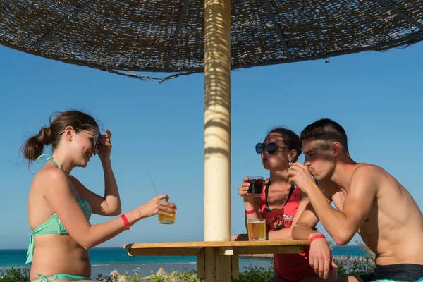 Grup genç çekici arkadaşıyla kokteyl içme ve gülümseyen kumsalda eğlenceli yaşıyorsanız