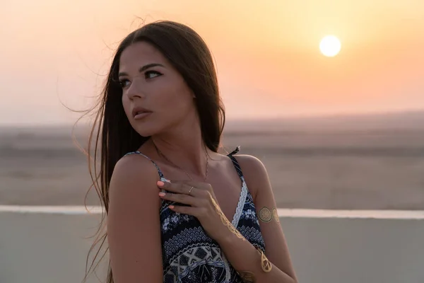 Une belle fille vêtue de style arabe, debout sur le toit au coucher du soleil. En arrière-plan, le désert et le soleil — Photo