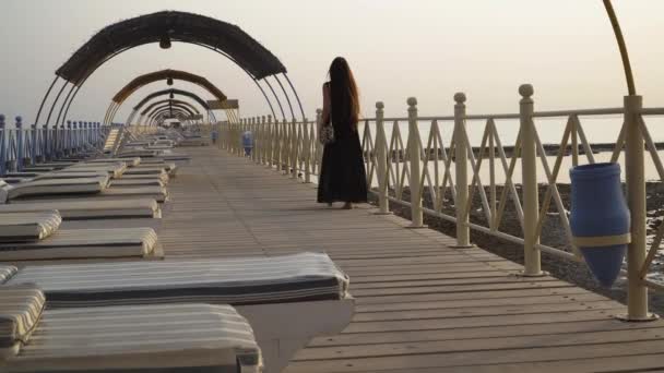 A girl in a bathing suit and a cloak is walking along the pier at dawn. — Stock Video