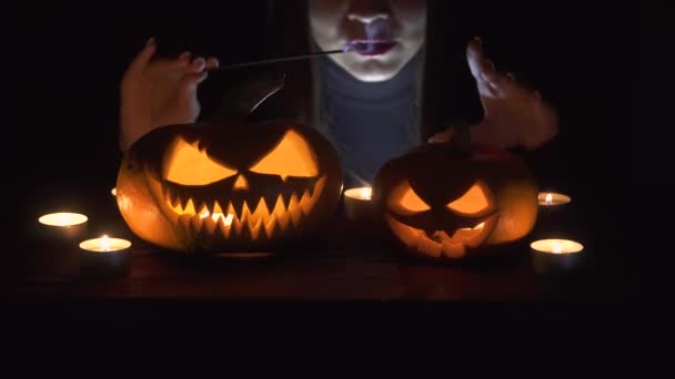 Nos principais termos da abóbora, bruxa lança um feitiço por trás.. Mulher bonita em chapéu de bruxa e traje segurando abóbora esculpida. Design de arte Halloween . — Vídeo de Stock