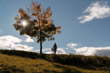 Kız bir tepede yalnız bir ağaç yanında duruyor