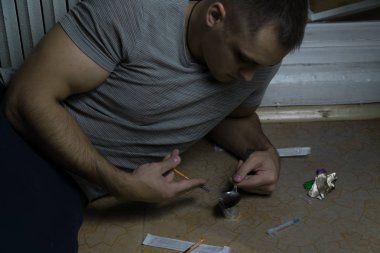 Uyuşturucu bağımlısı olan bir adamı yere oturur ve bir kaşık bir doz üzerinde bir mum hazırlar