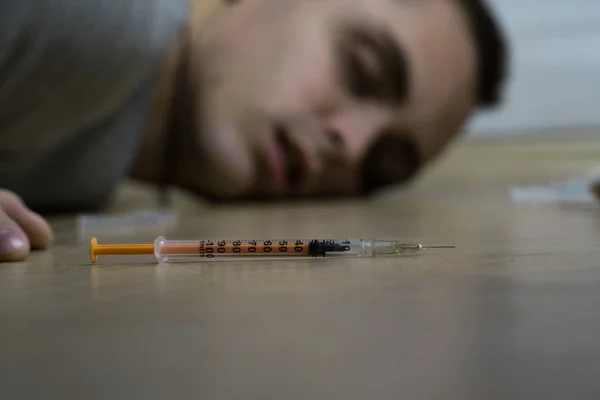 The syringe lies on the floor. Behind is a drug addict. Death of a drug addict