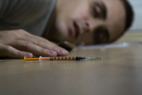 The syringe lies on the floor. Behind is a drug addict. Death of a drug addict