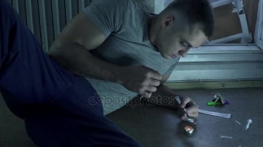 Uyuşturucu bağımlısı olan bir adamı yere oturur ve bir kaşık bir doz üzerinde bir mum hazırlar.