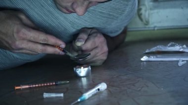 Uyuşturucu bağımlısı olan bir adamı yere oturur ve bir kaşık bir doz üzerinde bir mum hazırlar.