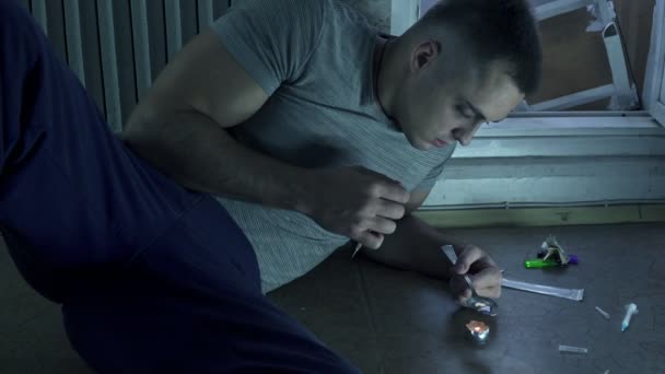 Een man die verslaafd aan de drugs is zit op de vloer en bereidt een dosis in een lepel op een kaars. — Stockvideo
