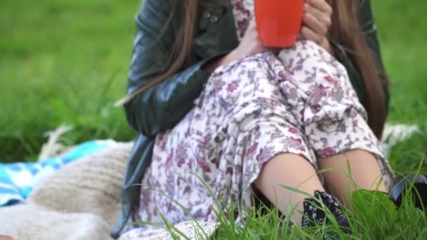 En tjej dricker varmt te medan du sitter på gräset nära floden. — Stockvideo
