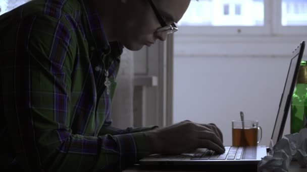 Um escritor ou um programador trabalha em casa para um laptop não para o primeiro dia. Um homem fica com raiva e começa a fumar um cigarro. Na mesa estão garrafas com cerveja, chá, cigarros, papel — Vídeo de Stock