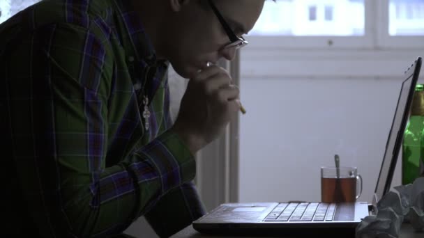 Een schrijver of een programmeur werkt thuis voor een laptop niet voor de eerste dag. Een man wordt boos en begint met het roken van een sigaret. Op de tafel zijn flessen met bier, thee, sigaretten, papier — Stockvideo