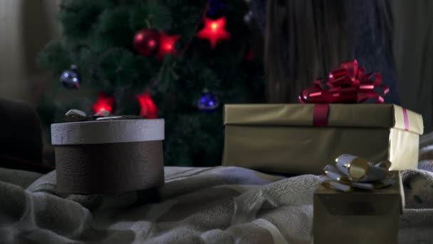 Новогодние подарки на переднем плане, а девушка украшает елку на спине — стоковое видео