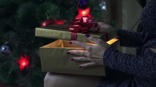 Девушка держит в руках подарок, сидит под елкой — стоковое видео