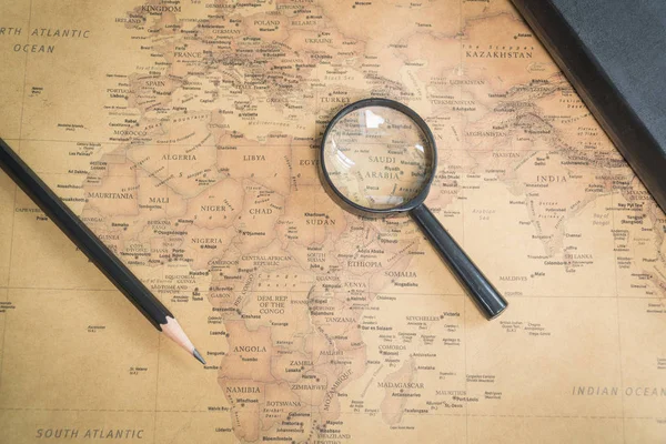 An old world map, a magnifying glass, a pencil and a notepad.