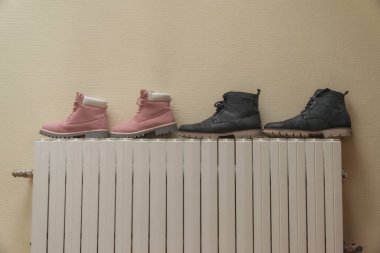 Winter boots are dried on the battery near the wall clipart
