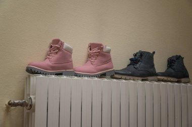 Winter boots are dried on the battery near the wall clipart