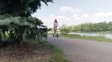 Çok ırklı bir kız nehir boyunca elektrikli scooter kullanıyor..