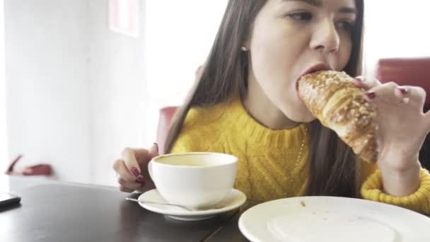 Meisje bijt een croissant in een koffieshop. Close-up. — Stockvideo