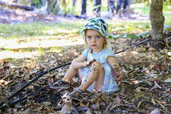 Симпатична маленька дівчинка сидить на землі, граючи в бруд — стокове фото