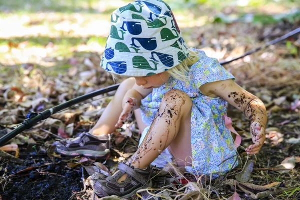 Cute little girl is sitting on the ground , playing in mud