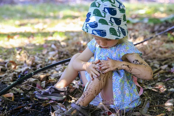 Милая маленькая девочка сидит на земле, играет в грязи — стоковое фото
