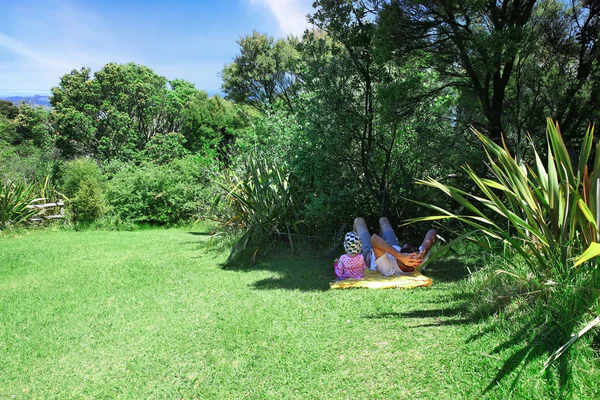 Ojciec i dziecko, leżąc na trawie w cieniu wierzchołki drzew — Zdjęcie stockowe