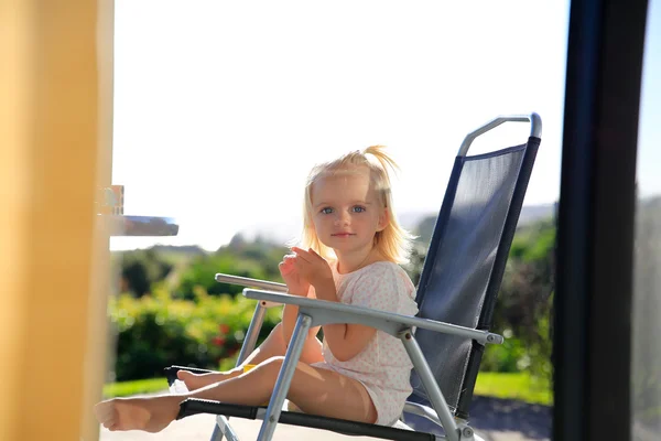 На відкритому повітрі фото милої маленької дівчинки, що має сонячну ванну на стільці — стокове фото