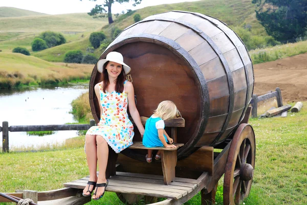 Улыбающаяся молодая женщина с дочерью, сидящей на деревянной бочке — стоковое фото