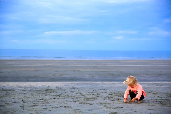Hermosa chica rubia sentada en la playa, jugando con arena . — Foto de Stock
