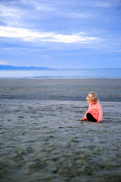 Bella ragazza dai capelli biondi seduta sulla spiaggia, che gioca con la sabbia . — Foto Stock