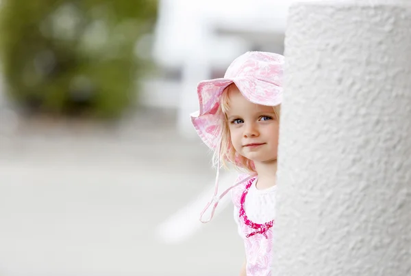 Чарівна маленька біла дівчинка в гарному капелюсі дивиться з білої колонки — стокове фото