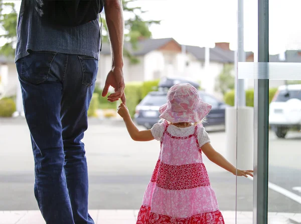 Маленькая девочка в розовом платье держит отца за руку, выходит — стоковое фото