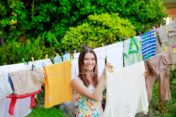 Smiling young woman hanging laundry on clothesline at the backyard — Stock Photo, Image