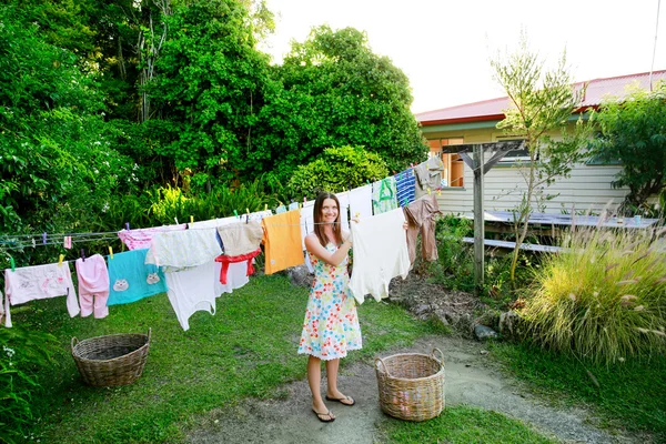 Smiling young woman hanging laundry on clothesline at the backyard — Stock Photo, Image